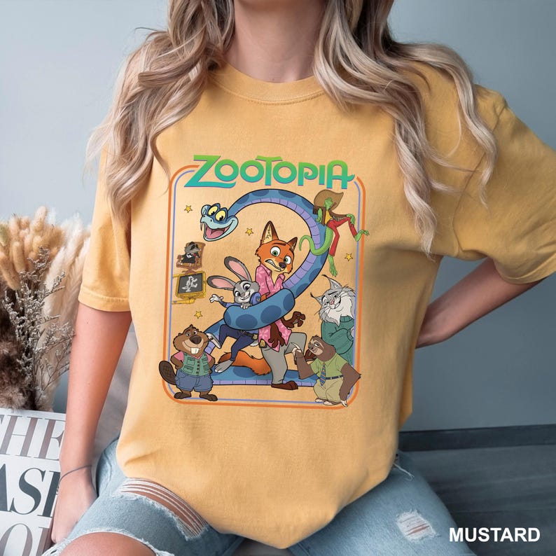 Puede incluir: Camiseta de color mostaza con un gr&aacute;fico de la pel&iacute;cula Zootopia. El dise&ntilde;o incluye el t&iacute;tulo de la pel&iacute;cula y varios personajes, como un zorro, un conejo y un perezoso. La camiseta es de estilo casual, cuello redondo.