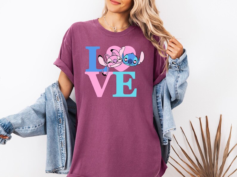 May include: A maroon t-shirt with the word "LOVE" in blue and pink block letters. The "O" is replaced by a pink heart with cartoon characters. A denim jacket is draped over the shoulders.