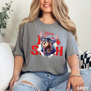 Puede incluir: Camiseta gris con un dise&ntilde;o de Stitch y un mono de Disney. El gr&aacute;fico muestra a Stitch rompiendo un efecto de papel rasgado, con las palabras "Disney" y "Lilo & Stitch" en rojo. La camiseta es de color gris liso.