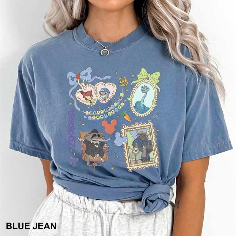Puede incluir: Camiseta azul vaquero con un gr&aacute;fico colorido de personajes e iconos enmarcados. El dise&ntilde;o incluye im&aacute;genes de un zorro, un conejo, una serpiente y un mapache. La palabra "zootopia" est&aacute; impresa verticalmente en el lado izquierdo de la camiseta.