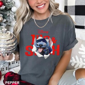 May include: Dark gray t-shirt featuring the Disney characters Lilo & Stitch. The design shows Stitch popping out of a torn paper effect, with the words "Lilo & Stitch" in red. The shirt has short sleeves and a relaxed fit.