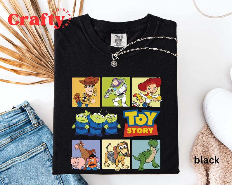 Pu&ograve; includere: Maglietta nera a tema Toy Story. La maglietta presenta un collage di personaggi del film, tra cui Woody, Buzz Lightyear, Jessie e gli alieni. Il testo "Toy Story" &egrave; stampato in lettere gialle sulla maglietta.