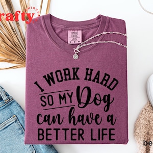 May include: A maroon t-shirt with the text "I work hard so my dog can have a better life" printed in black.