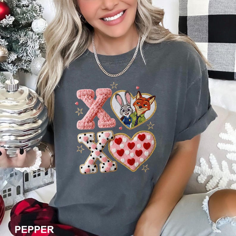 May include: Dark gray t-shirt featuring the characters Judy Hopps and Nick Wilde from Zootopia. The shirt has the letters "XO" with heart and star designs. The word "PEPPER" is printed at the bottom.