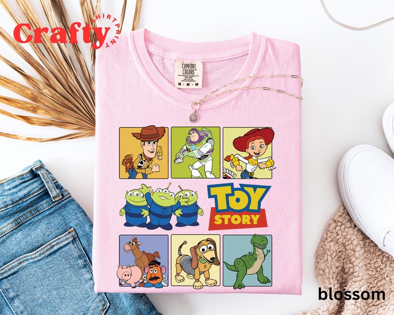 Pu&ograve; includere: Maglietta rosa con tema Toy Story. La maglietta presenta un collage di personaggi del film, tra cui Woody, Buzz Lightyear, Jessie e gli alieni. Il testo "Toy Story" &egrave; stampato in grassetto sulla maglietta.