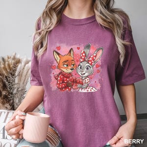 May include: Berry-coloured t-shirt with a cartoon fox and rabbit holding a heart-shaped gift box, surrounded by hearts. The fox wears a red scarf, and the rabbit has a bow. The word "BERRY" is printed at the bottom right.