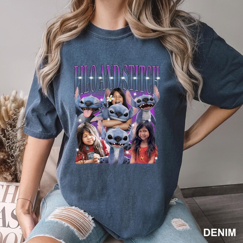 May include: Denim blue t-shirt featuring the text "Lilo and Stitch" above a graphic of the characters Lilo, Stitch, and two girls. The graphic has a purple background with white accents. The shirt is a casual style.