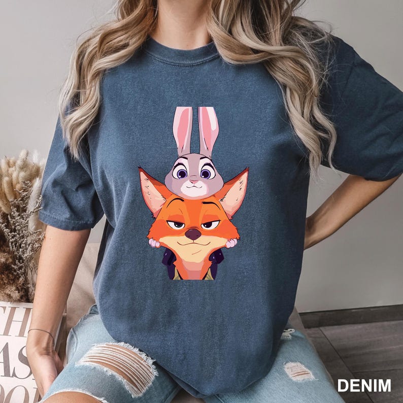 Puede incluir: Camiseta azul denim con una ilustraci&oacute;n de dibujos animados de un zorro y un conejo. El zorro es naranja, el conejo es gris. La palabra "DENIM" est&aacute; impresa en blanco en la esquina inferior derecha.