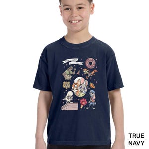 Puede incluir: Camiseta azul marino para ni&ntilde;os con personajes de dibujos animados y el texto "The Big Donut". El gr&aacute;fico incluye una rosquilla, una placa de polic&iacute;a y varios personajes de animales. La camiseta es de material suave.