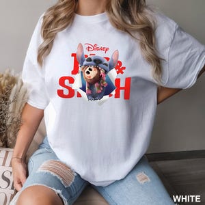 Puede incluir: Camiseta blanca con un dise&ntilde;o de Stitch de Lilo & Stitch de Disney. El dise&ntilde;o muestra a Stitch rompiendo la camiseta con las palabras "Lilo & Stitch" en rojo. La camiseta tiene un corte casual y oversize.