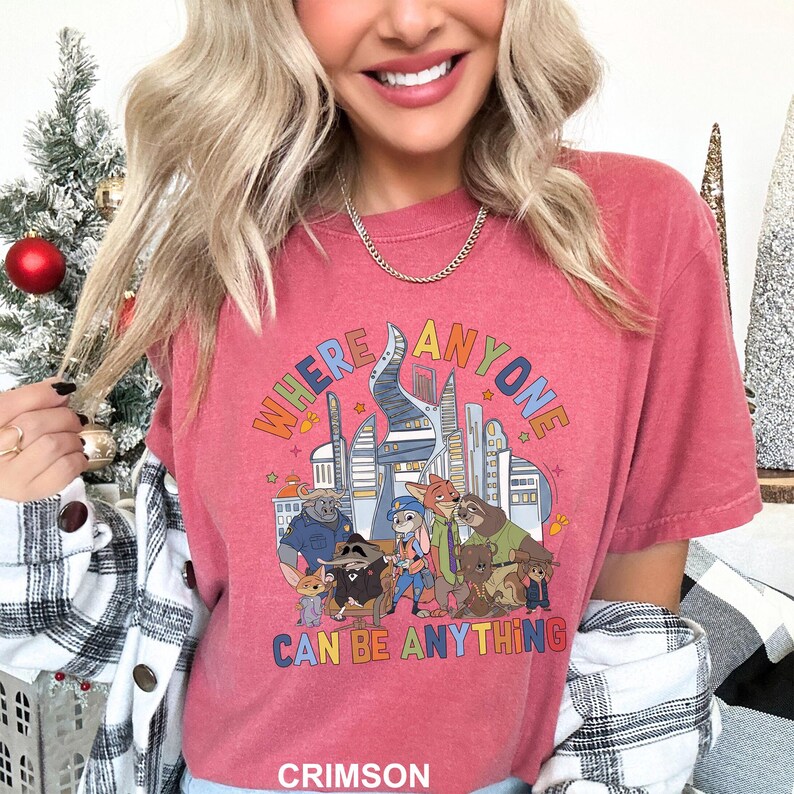 May include: Crimson-colored t-shirt featuring a colorful graphic with the text "WHERE ANYONE CAN BE ANYTHING" above a cartoon illustration of various animal characters and city buildings.