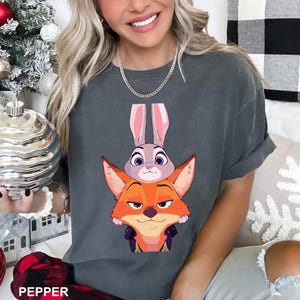 Puede incluir: Camiseta gris oscuro con un dise&ntilde;o de dibujos animados de un zorro y un conejo. El zorro es naranja y el conejo es gris con orejas rosas. La palabra "PEPPER" est&aacute; impresa en la parte inferior de la imagen. Una camiseta casual y c&oacute;moda.
