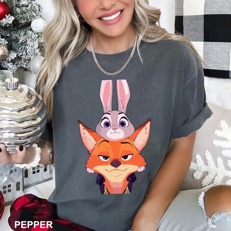 Puede incluir: Camiseta gris oscuro con un dise&ntilde;o de dibujos animados de un zorro y un conejo. El zorro es naranja y el conejo es gris con orejas rosas. La palabra "PEPPER" est&aacute; impresa en la parte inferior de la imagen. Una camiseta casual y c&oacute;moda.