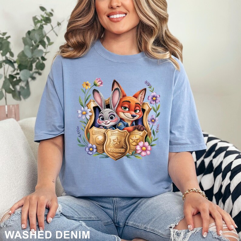 Pu&ograve; includere: T-shirt azzurra con una grafica colorata di Judy Hopps e Nick Wilde di Zootopia, incorniciata da fiori e distintivi della polizia. La maglietta &egrave; realizzata in materiale morbido ed &egrave; etichettata "WASHED DENIM".