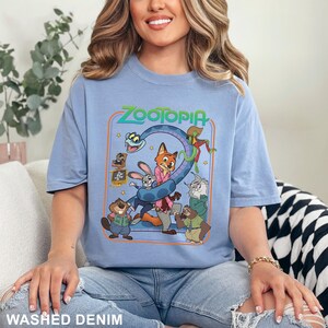 Puede incluir: Camiseta azul claro de manga corta con un gr&aacute;fico colorido de la pel&iacute;cula animada "Zootopia". El dise&ntilde;o incluye el t&iacute;tulo de la pel&iacute;cula y varios personajes. La camiseta est&aacute; hecha de un material suave y est&aacute; etiquetada como "Washed Denim".