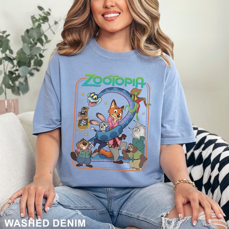 Puede incluir: Camiseta azul claro de manga corta con un gr&aacute;fico colorido de la pel&iacute;cula animada "Zootopia". El dise&ntilde;o incluye el t&iacute;tulo de la pel&iacute;cula y varios personajes. La camiseta est&aacute; hecha de un material suave y est&aacute; etiquetada como "Washed Denim".