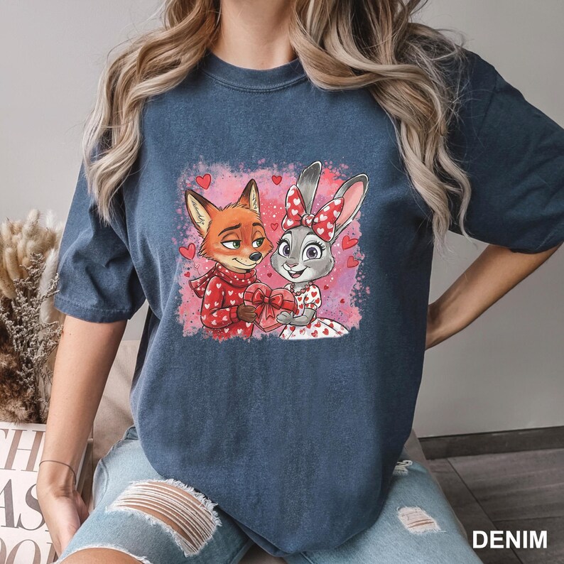 May include: Denim blue t-shirt with a cartoon image of a fox and a rabbit, both holding a heart-shaped gift. The fox is in a red sweater with white hearts, and the rabbit wears a dress with heart patterns. The word "DENIM" is printed on the bottom right.