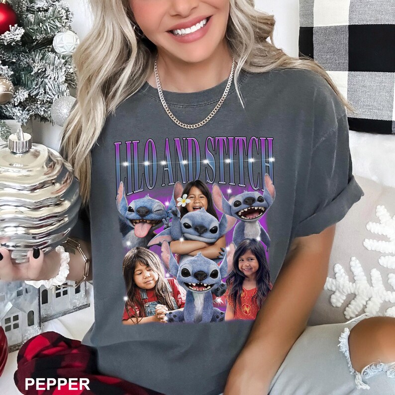 May include: Dark gray t-shirt featuring the text "Lilo and Stitch" in a purple and blue font. The shirt has a graphic of the characters Lilo and Stitch with two girls. The shirt is a relaxed fit.