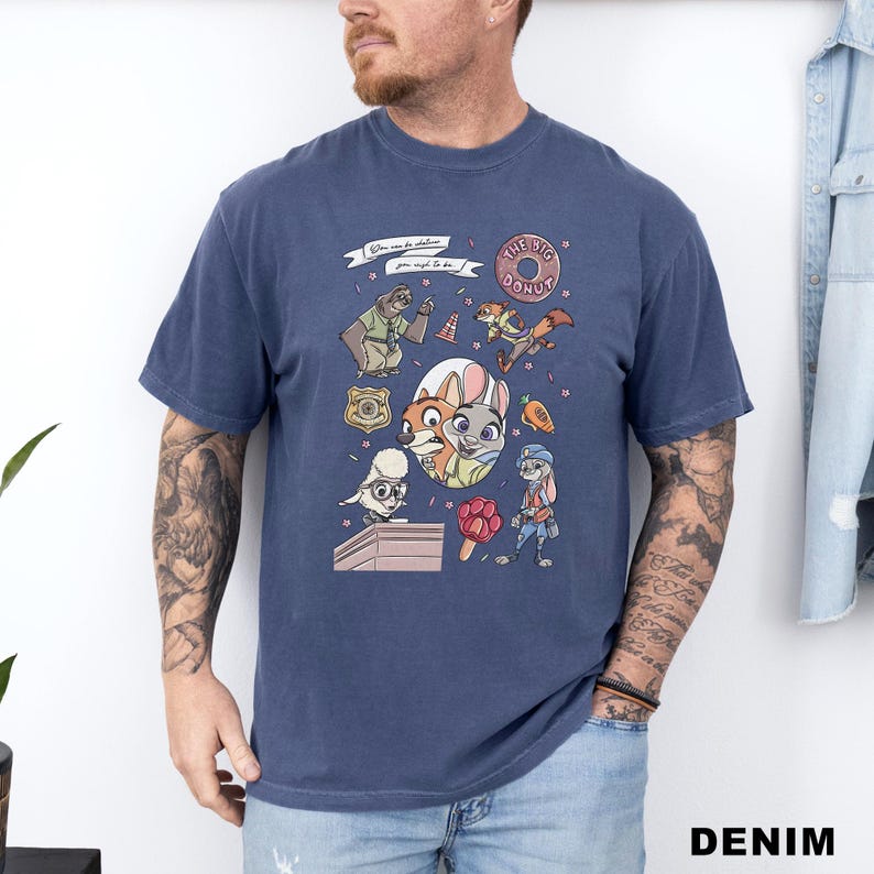 Puede incluir: Camiseta azul marino con personajes de dibujos animados y el texto "You can be anything you want to be." El dise&ntilde;o incluye una rosquilla, una placa de polic&iacute;a y varios personajes de animales. La camiseta es de material suave.