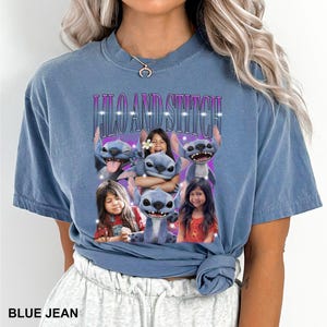 May include: Blue jean t-shirt featuring the text "Lilo and Stitch" in a purple and white font. The shirt has a graphic of the character Stitch and children. The shirt is a light blue color.