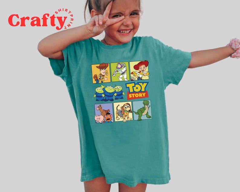 Pu&ograve; includere: Una maglietta blu turchese con una stampa grafica di personaggi del film Toy Story. La grafica include Woody, Buzz Lightyear, Rex e altri personaggi. Il testo "Toy Story" &egrave; stampato sotto la grafica.