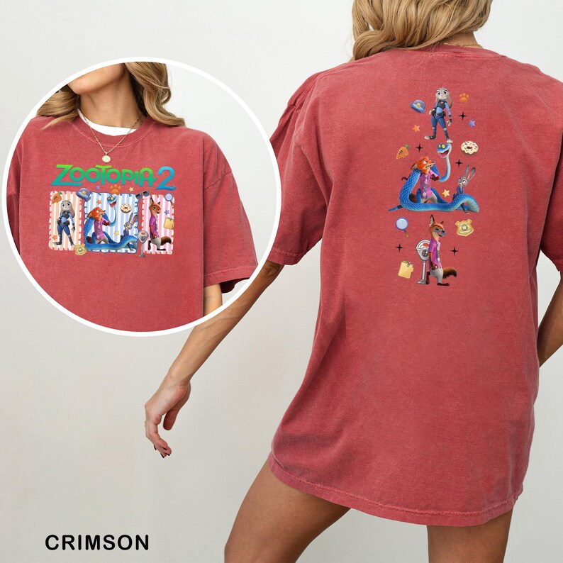 May include: Crimson-colored t-shirt featuring a colorful graphic from "Zootopia 2" on the front and back. The front graphic displays characters and the movie title. The back graphic shows characters and themed elements. The shirt is a comfortable, casual style.