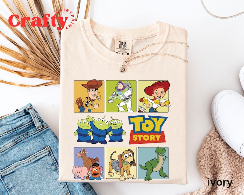 Pu&ograve; includere: Una maglietta beige a tema Toy Story. La maglietta presenta una griglia di nove quadrati con diversi personaggi del film, tra cui Woody, Buzz Lightyear, Jessie e i tre piccoli alieni verdi. Il testo "Toy Story" &egrave; stampato in un font rosso e bianco.