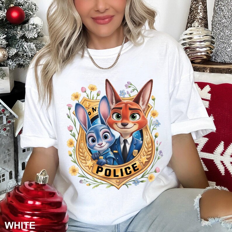 May include: White t-shirt featuring a cartoon illustration of two characters from the movie Zootopia, a fox and a bunny, inside a police badge. The badge is surrounded by flowers and the word "POLICE" is printed below the characters.