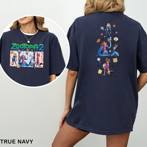 May include: True navy blue t-shirt featuring the text "ZOOTOPIA 2" with cartoon characters on the front. The back of the shirt has a vertical design with more cartoon characters and icons. The shirt is made of a soft material.