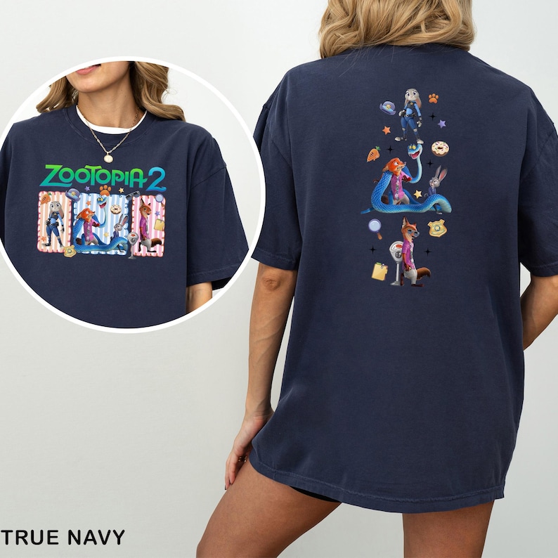 May include: True navy blue t-shirt featuring the text "ZOOTOPIA 2" with cartoon characters on the front. The back of the shirt has a vertical design with more cartoon characters and icons. The shirt is made of a soft material.