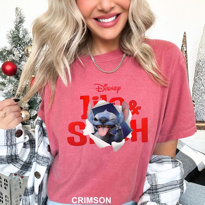 May include: Crimson-colored t-shirt featuring the Disney logo and the words "Lilo & Stitch" in red. The shirt has a graphic of Stitch popping out of a torn paper effect, with his tongue out and a peace sign.