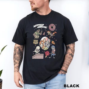 Puede incluir: Camiseta negra con personajes de dibujos animados y el texto "You can be whatever you wish to be" y "THE BIG DONUT". El dise&ntilde;o incluye una rosquilla, una zanahoria y varios personajes.