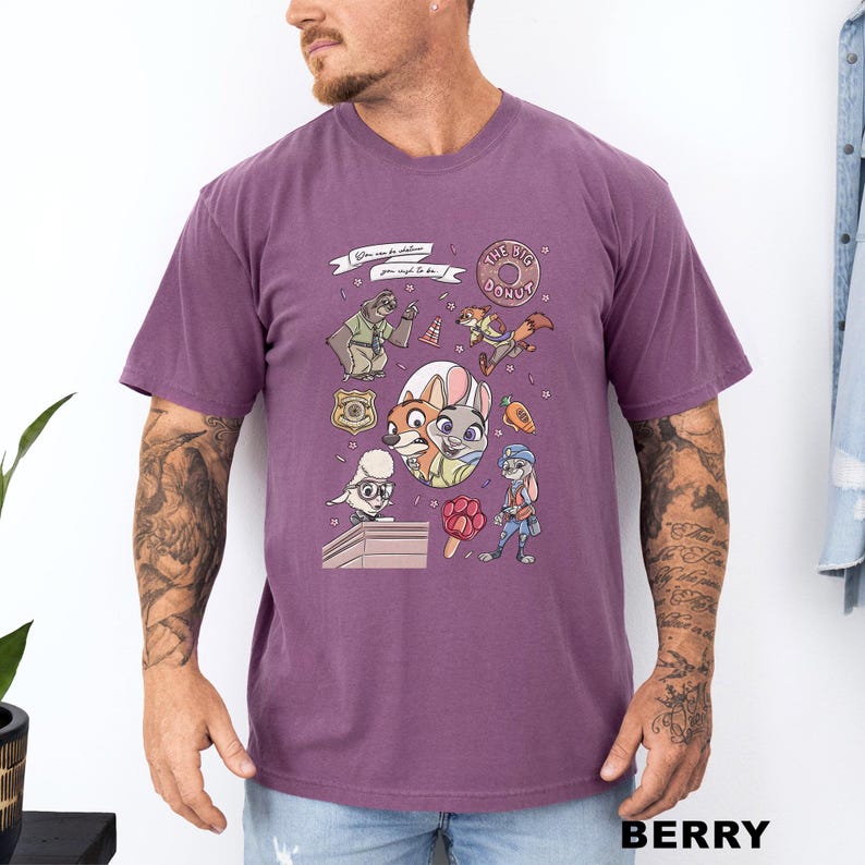 Puede incluir: Camiseta de color bayas con personajes de dibujos animados y el texto "When you're in Zootopia, you wish to be...". La camiseta tiene cuello redondo y mangas cortas. El gr&aacute;fico incluye una rosquilla, una placa de polic&iacute;a y varios personajes de animales.