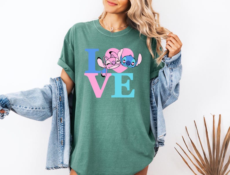 May include: Green t-shirt with the word "LOVE" in blue and pink letters. The "O" is a pink heart with cartoon characters. The shirt is worn with a denim jacket.