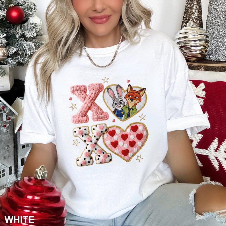 May include: White t-shirt with a Valentine's Day design. The design includes the letters X and O, a heart-shaped image of Judy Hopps and Nick Wilde, and a heart filled with red hearts. The letters are in pink and black.