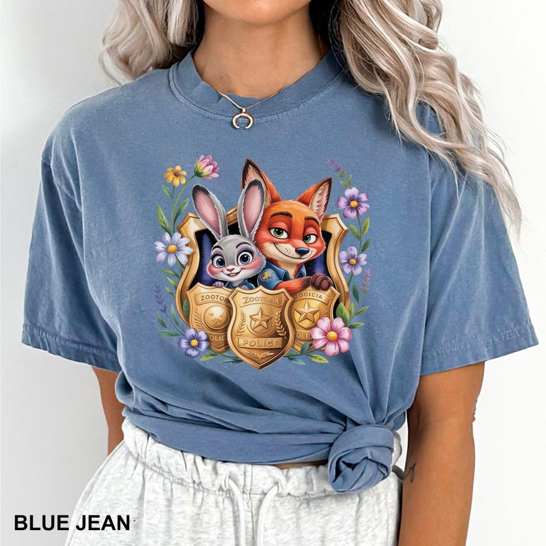 Pu&ograve; includere: T-shirt blu jeans con una grafica colorata di Judy Hopps e Nick Wilde di Zootopia, incorniciata da fiori e distintivi della polizia. Il testo "Zootopia Police" &egrave; visibile sui distintivi. La maglietta ha una vestibilit&agrave; rilassata.