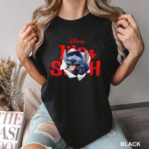 May include: Black t-shirt featuring the Disney characters Lilo & Stitch. The red text "Disney Lilo & Stitch" is printed on the front, with Stitch bursting through a torn paper effect. The word "BLACK" is printed at the bottom.