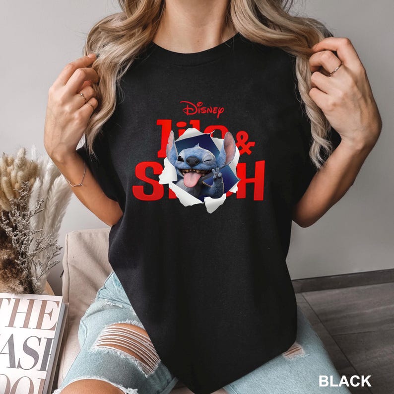 May include: Black t-shirt featuring the Disney characters Lilo & Stitch. The red text "Disney Lilo & Stitch" is printed on the front, with Stitch bursting through a torn paper effect. The word "BLACK" is printed at the bottom.