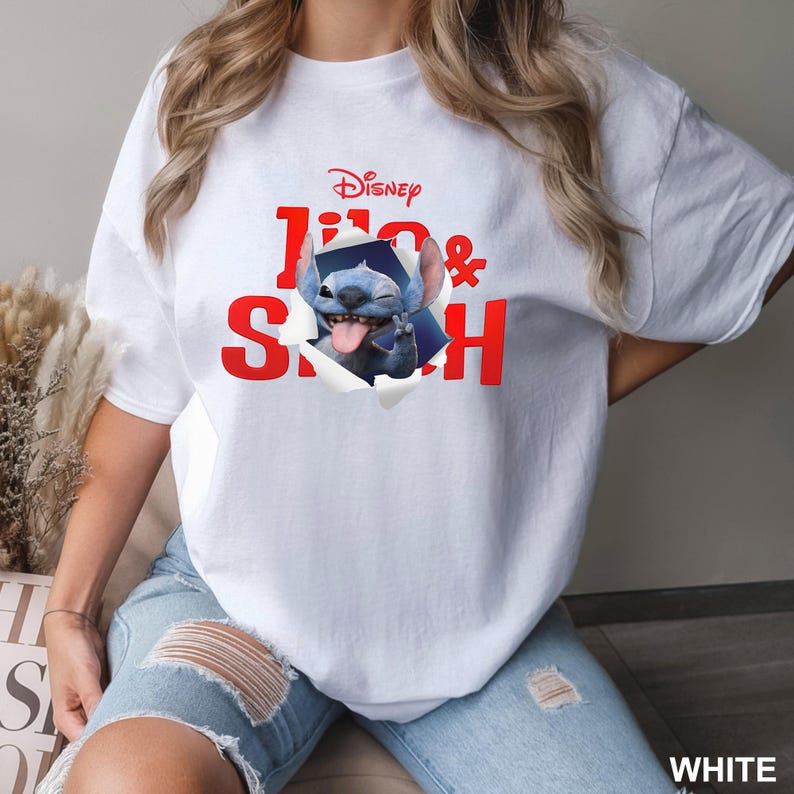 May include: White t-shirt featuring the Disney characters Stitch, with the text "Lilo & Stitch" in red. The graphic shows Stitch bursting through a torn section of the shirt. The word "Disney" is above the text.