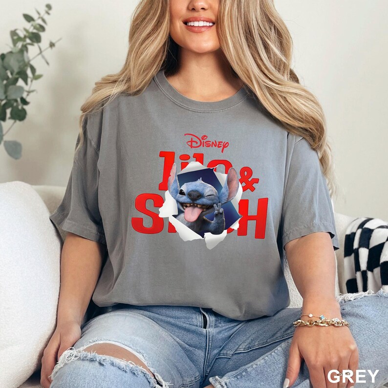 May include: Grey t-shirt featuring the Disney characters Lilo & Stitch. The design shows Stitch wearing a graduation cap, bursting through a torn paper effect. The text "Disney Lilo & Stitch" is in red.
