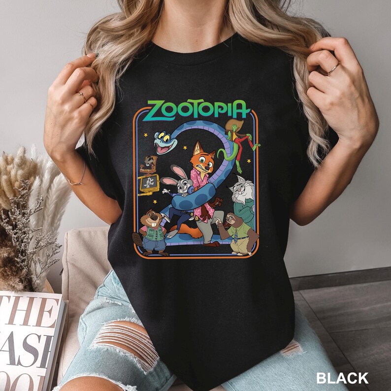 Puede incluir: Camiseta negra con un gr&aacute;fico colorido de "Zootopia". El dise&ntilde;o presenta personajes de la pel&iacute;cula animada, como un zorro, un conejo y un perezoso, junto con el t&iacute;tulo de la pel&iacute;cula. La camiseta tiene cuello redondo y mangas cortas.