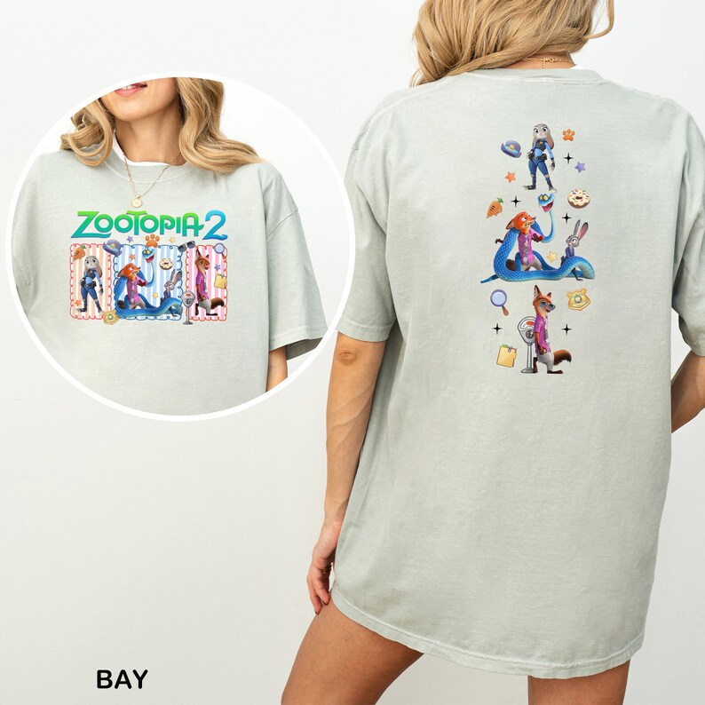 May include: A light green t-shirt featuring the text "ZOOTOPIA 2" with cartoon characters. The back of the shirt has a vertical design with more cartoon characters and icons. The shirt is a comfortable, oversized fit.