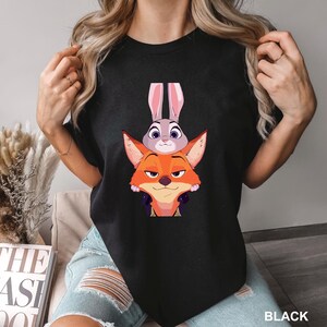 Puede incluir: Camiseta negra de cuello redondo con una ilustraci&oacute;n de dibujos animados de un zorro y un conejo. El zorro es naranja y el conejo es gris. El texto "BLACK" est&aacute; en la esquina inferior derecha de la camiseta.