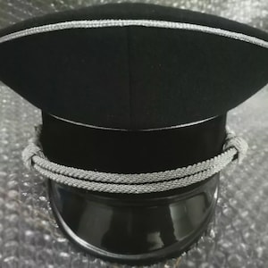 May include: A black hat with silver trim and a silver rope detail. The hat has a shiny black brim. The hat is a military style hat.