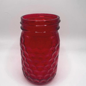 May include: A red glass jar with a textured, diamond-like pattern. The jar has a wide mouth and a screw-on rim. The jar is likely used for canning or storage. The jar is approximately 5 inches tall.