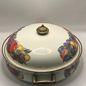 May include: Cream-colored oval casserole dish with a lid, featuring a colorful fruit design around the rim. The dish has gold-colored handles and a gold-colored knob on the lid. The fruit design includes grapes, apples, and pears.