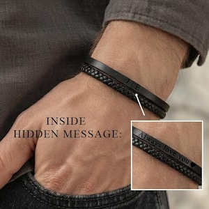 May include: A black leather bracelet featuring a braided texture and a smooth metal bar engraved with the letters JE. An inset shows the inside of the bracelet with the engraved text Always love you and a small heart symbol on the metal bar.
