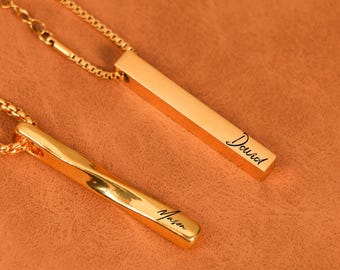 Könnte beinhalten: Zwei goldfarbene Halsketten mit Stäben und Kettengliedern. Eine Halskette trägt den eingravierten Namen "David", die andere den Namen "Mason". Die Halsketten werden auf einer braunen Oberfläche präsentiert.