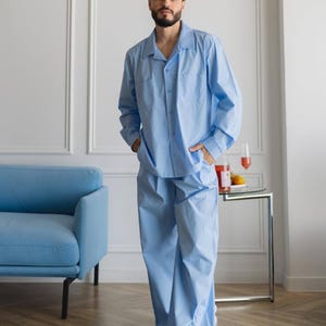 Könnte beinhalten: Ein hellblaues Pyjama-Set bestehend aus einem langärmeligen Hemd mit Knopfleiste, Kragen und zwei Brusttaschen sowie einer passenden, locker sitzenden Hose. Der Stoff besteht aus einfarbiger, glatter hellblauer Baumwolle mit schlichtem Design.