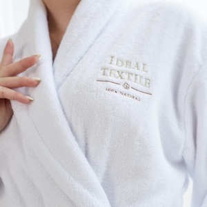 May include: White bathrobe with a large collar and a belt. The robe has the text "IDEAL TEXTILE 100% NATURAL" embroidered on the front.